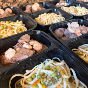 Steak, shrimp, pasta, and vegetables portioned into meal-prep trays