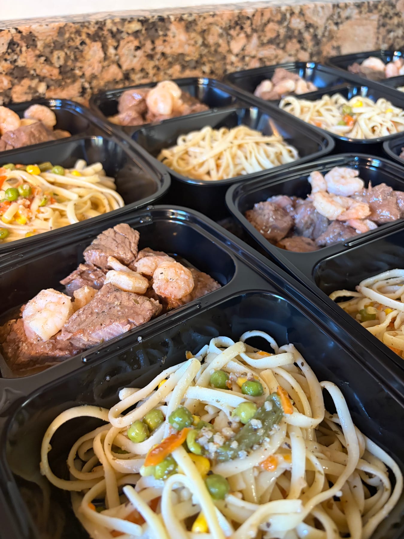 Steak, shrimp, pasta, and vegetables portioned into meal-prep trays